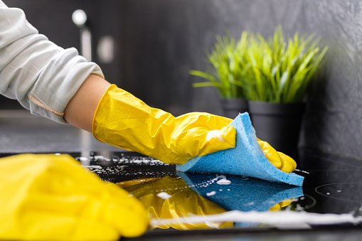 the girl washes the stove with a blue sponge in yellow gloves